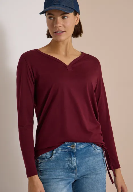 Shirt mit Split Neck im Tunika-Look red wine Frau trägt burgunderfarbenes Langarmshirt mit V-Ausschnitt und Tunnelzug, blaue Jeans und Cap.