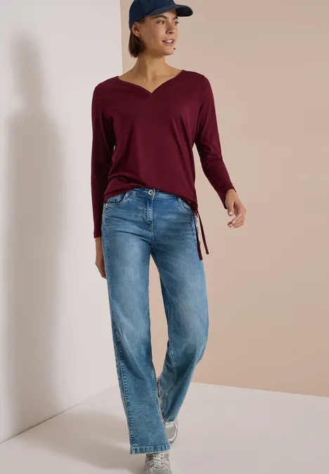 Shirt mit Split Neck im Tunika-Look red wine Frau mit Jeans, weinrotem V-Pullover, Baseballcap und Sneakers vor neutralem Hintergrund.