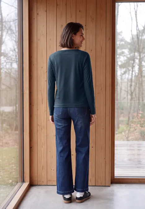 Shirt mit Split Neck im Tunika-Look moonlight blue Frau steht von hinten in einem Raum vor großen Glasfenstern, trägt grünen Pullover und Jeans.