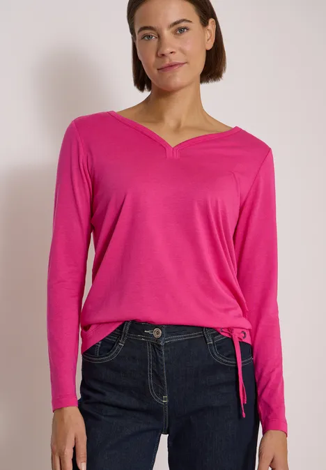 Shirt mit Split Neck im Tunika-Look pink flash Frau in pinkem V-Ausschnitt-Oberteil und dunklen Jeans vor neutralem Hintergrund.