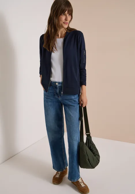 Ottoman Blouson in Unifarbe urban dark blue Frau in weißem T-Shirt, dunkelblauer Strickjacke, weiten Jeans, braunen Sneakern, grünem Schulterbeutel.