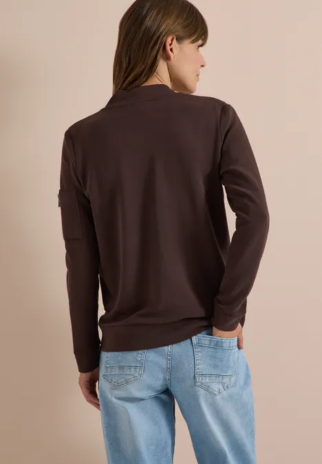 Ottoman Blouson in Unifarbe truffle brown Eine Frau von hinten mit braunem Langarmshirt und hellblauen Jeans vor beigem Hintergrund.