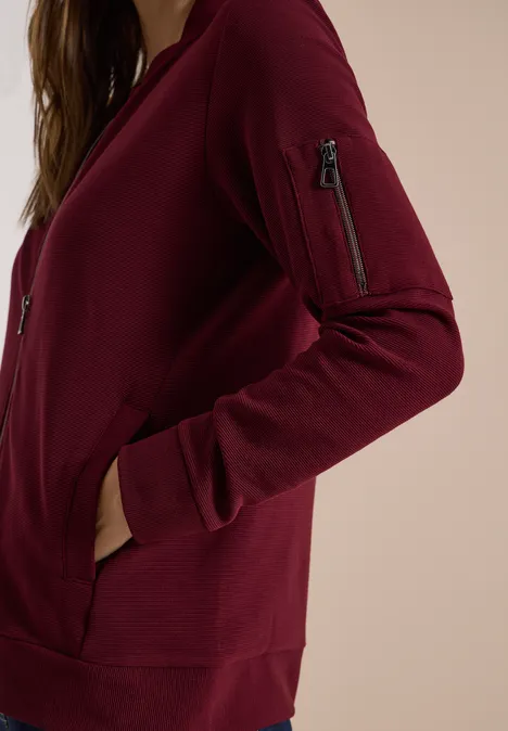 Ottoman Blouson in Unifarbe red wine Seitliche Nahaufnahme einer Person in einem weinroten Sweatshirt mit Reißverschlusstaschen auf dem Oberarm