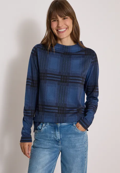 Shirt met lange mouwen, trechterhals en patroon urban dark blue melange Eine Frau lächelt in einem blauen, karierten Langarmshirt und blauen Jeans vor hellem Hintergrund.