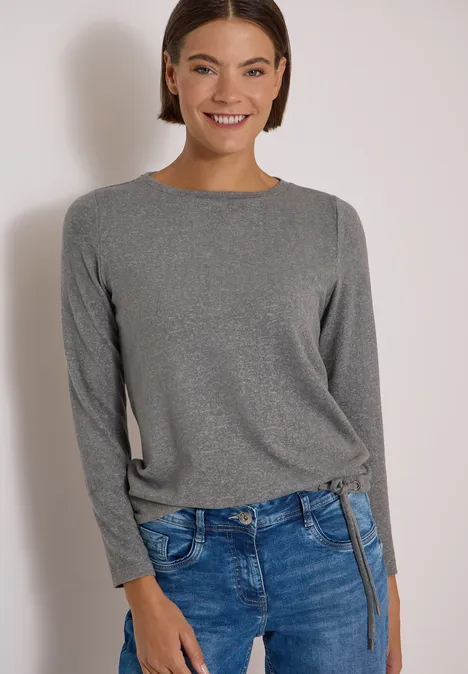 Uśmiechnięta kobieta w szarej bluzce i niebieskich jeansach.