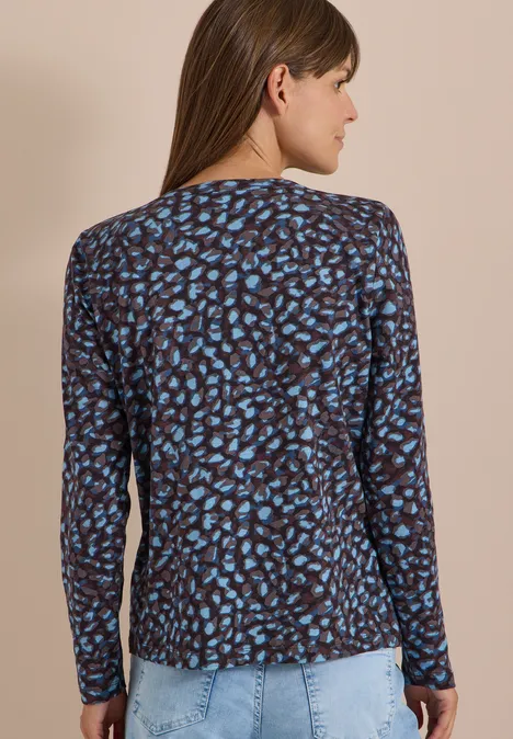 Femme de dos portant un haut à manches longues bleu et noir à motif et un jean clair.