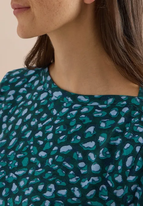 Une femme porte un haut bleu-vert à motif léopard abstrait