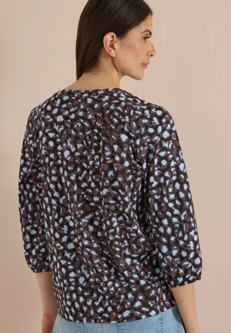 Femme de dos portant un chemisier marron foncé à imprimé taches bleues, manches 3/4, coupe décontractée.