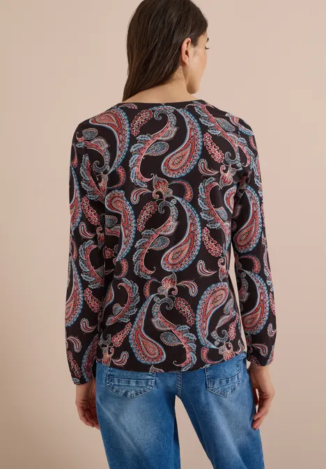 Frau von hinten in blauer Jeans und langärmeligem Oberteil mit buntem Paisley-Muster.