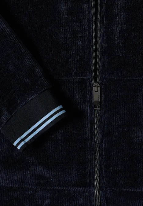 Detail einer dunkelblauen Samtjacke mit Reißverschluss und Ärmelsaum mit zwei hellblauen Streifen.