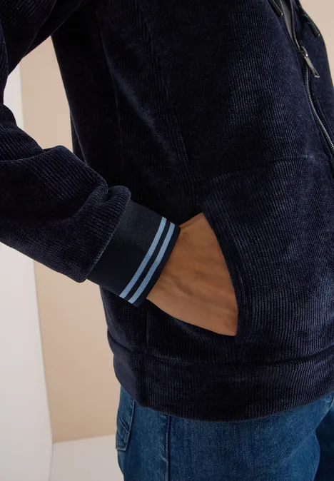 Seitliche Nahaufnahme: Person trägt dunkelblaue Fleecejacke mit Reißverschluss und Hand in Tasche, blaue Jeans.