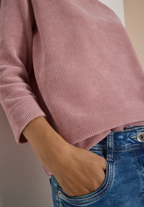 Nahaufnahme einer Person mit rosa Pullover und blauer Jeans, Hand in Hosentasche.