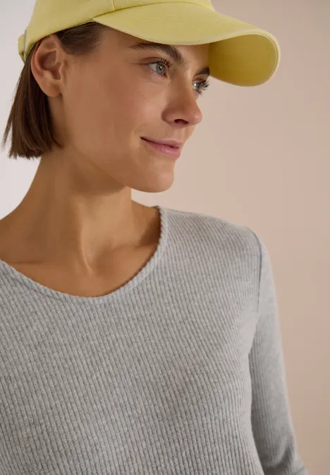 Junge Frau mit gelber Baseballkappe und grauem Oberteil, lächelnd, seitliches Porträt.