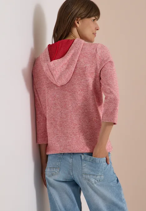 Femme de dos portant un gilet à capuche rose en maille à manches 3/4 et un jean bleu clair ample.