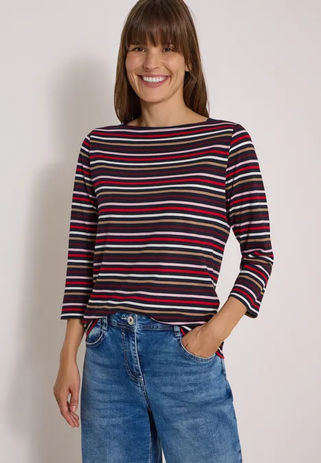 Femme souriante porte un haut rayé et un jean bleu.