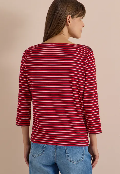 Femme de dos portant un t-shirt à manches 3/4 rayé rouge et noir avec un jean, fond clair.