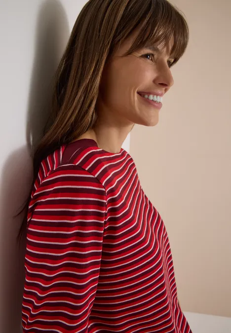 Portrait de profil d'une femme souriante, pull rayé rouge et blanc, fond clair.
