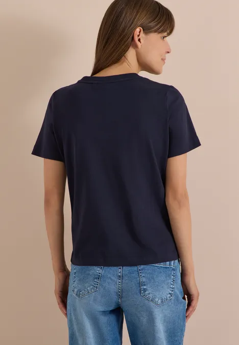 Personne de dos en t-shirt bleu marine et jean sur fond beige.