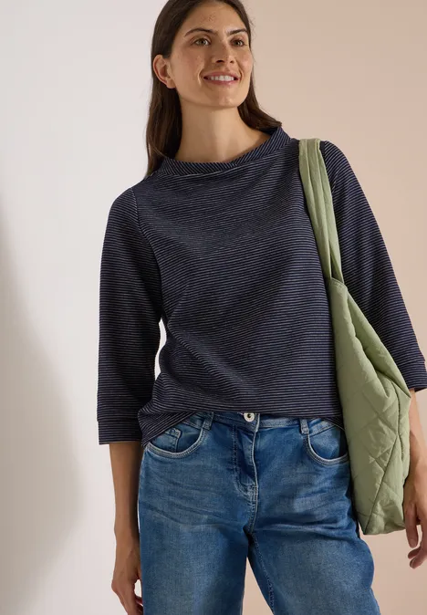 Ottoman Shirt im Two-Tone-Look urban dark blue Junge Frau in Jeans und dunkelblauem Pullover trägt eine grüne Umhängetasche und lächelt.