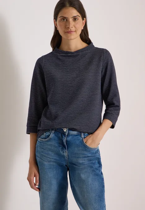 Ottoman Shirt im Two-Tone-Look urban dark blue Frau steht lässig in Jeans und dunkelblauem Langarmshirt, eine Hand locker in der Hosentasche.