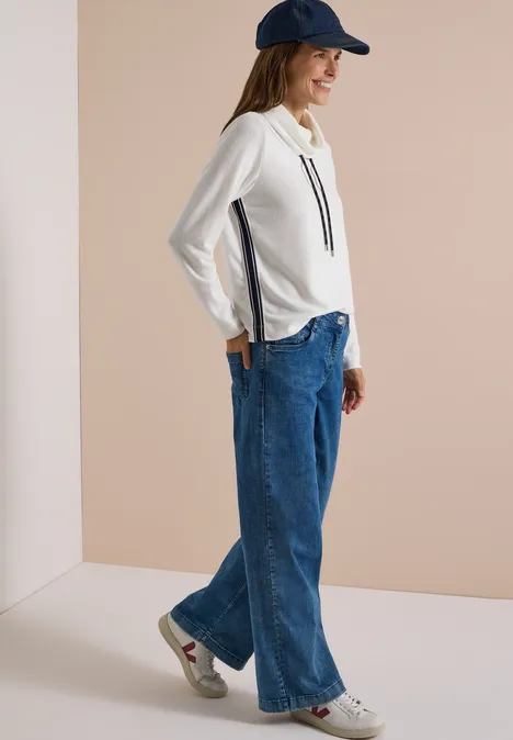 Zacht shirt met kraag en band vanilla white Frau in seitlicher Pose trägt cremefarbenes Sweatshirt, weite Jeans, weiße Sneaker und blaue Baseballkappe.