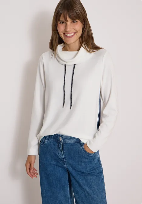 Zacht shirt met kraag en band vanilla white Lächelnde Frau in weißem Rollkragenpullover mit schwarzen Kordeln und Jeans vor hellem Hintergrund.