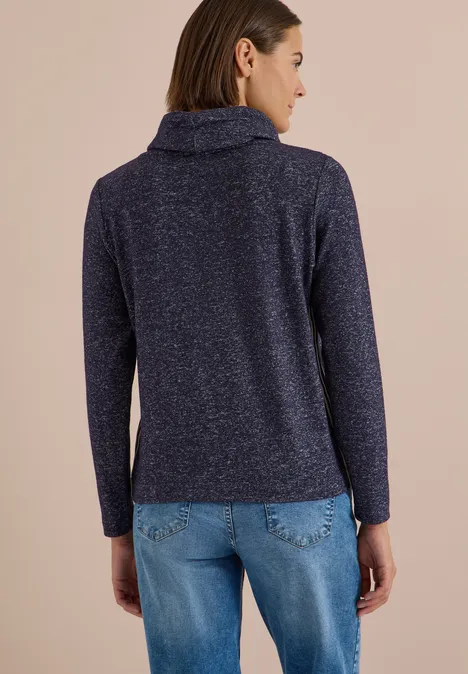 Vue de dos d’une femme en pull bleu marine à col roulé et jean clair sur fond beige.