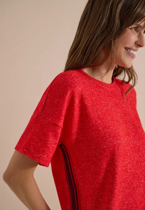 Frau in rotem kurzärmligem Pullover mit seitlichem Streifendetail, lächelnd im Profil.