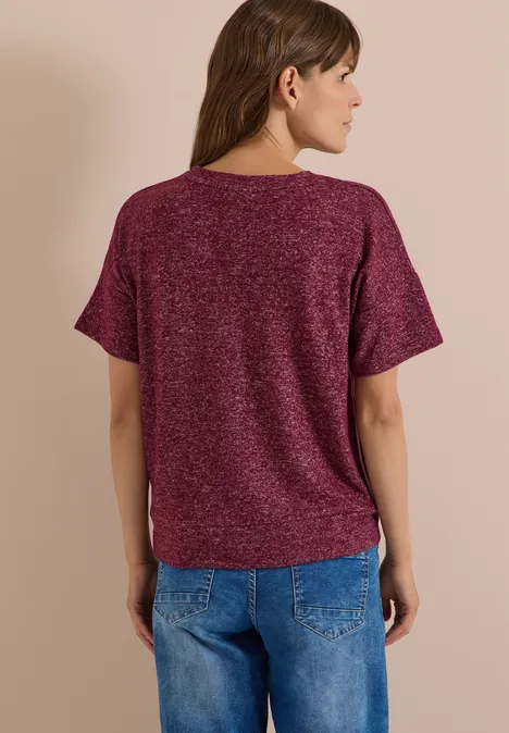 Frau von hinten trägt bordeauxfarbenes T-Shirt mit kurzen Ärmeln und blaue Jeans.