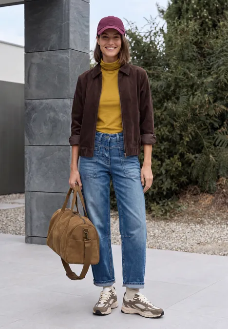 Langarm Shirt in Unifarbe mit Turtle Neck golden honey Junge Frau in gelbem Rollkragenpullover, brauner Jacke, Jeans, Sneakers und Mütze hält einen Rucksack.