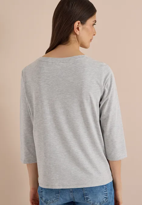 Femme de profil portant un haut gris à manches 3/4, fond neutre