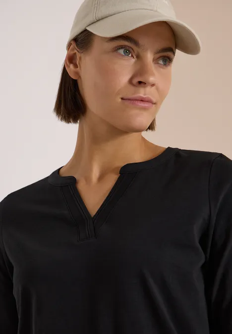 Eine Frau in schwarzem V-Neck-Oberteil und beiger Baseballmütze blickt seitlich.