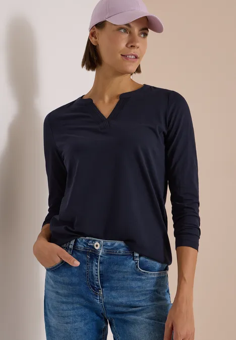 Frau in lässigem Outfit mit dunklem Langarmshirt, Jeans und Baseballcap.