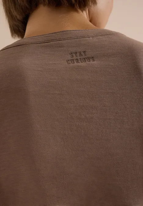 Person von hinten in braunem T-Shirt mit kleinem 'STAY STRONG'-Aufdruck am Nacken.