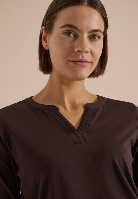 Eine Frau mit kurzem braunen Haar und dunkelbraunem Shirt, schaut frontal in die Kamera.