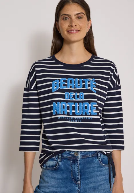 3/4-Arm Shirt Boat Neck und Streifen urban dark blue Eine Frau trägt ein blau-weiß gestreiftes Shirt mit 'Beauty of the Nature'-Aufdruck und Jeans.