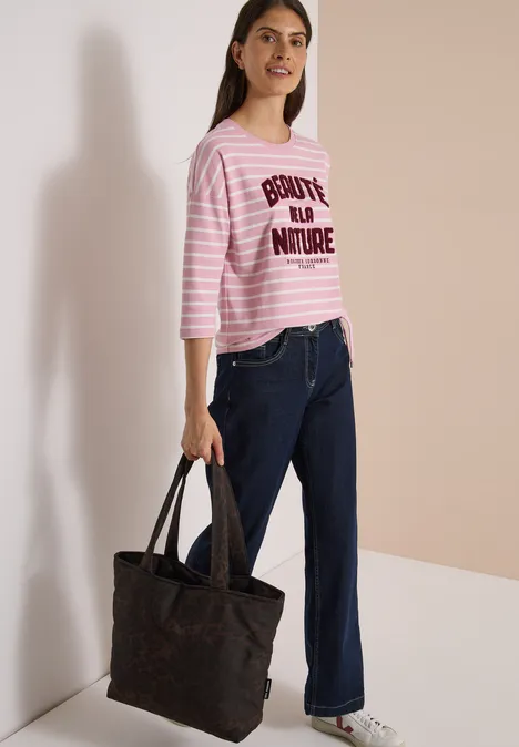 Frau in rosa-weiß gestreiftem Shirt mit 'BONJOUR LA NATURE', weiten Jeans und schwarzer Tasche