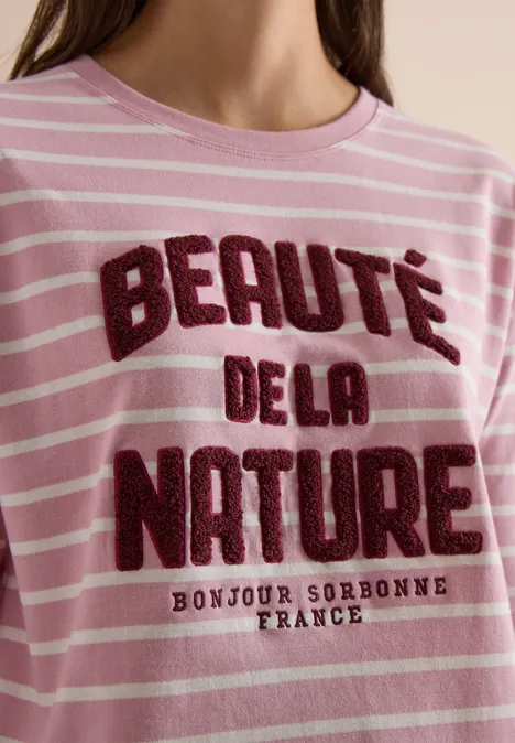 Trägt ein rosa-weiß gestreiftes Shirt mit Aufschrift 'Beauté de la Nature' und 'Bonjour Sorbonne France'.