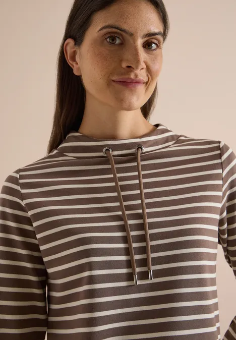 Portrait d'une femme souriante en sweat à capuche rayé.