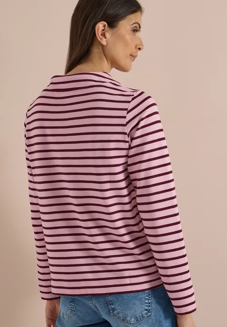Eine Frau ist von hinten zu sehen und trägt ein rosa-schwarz gestreiftes Langarmshirt und blaue Jeans.