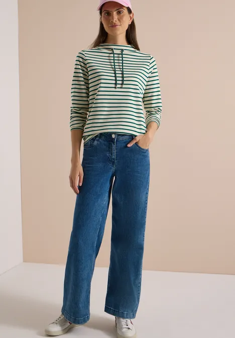 Frau in gestreiftem Langarmshirt, weitem Jeans und Cap.