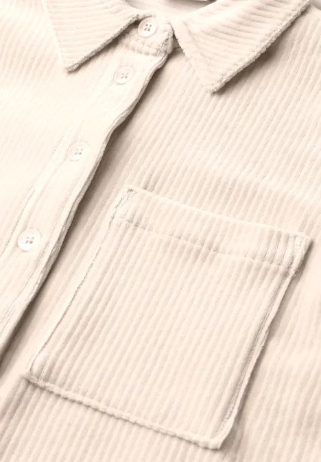 Gros plan sur une chemise beige en velours côtelé avec patte de boutonnage, col et poche poitrine.