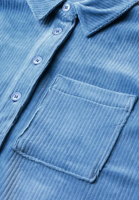 Jersey-corduroyblouse met halflange mouwen in effen kleur north blue Close-up van een lichtblauw corduroy overhemd met knoopsluiting en borstzak.