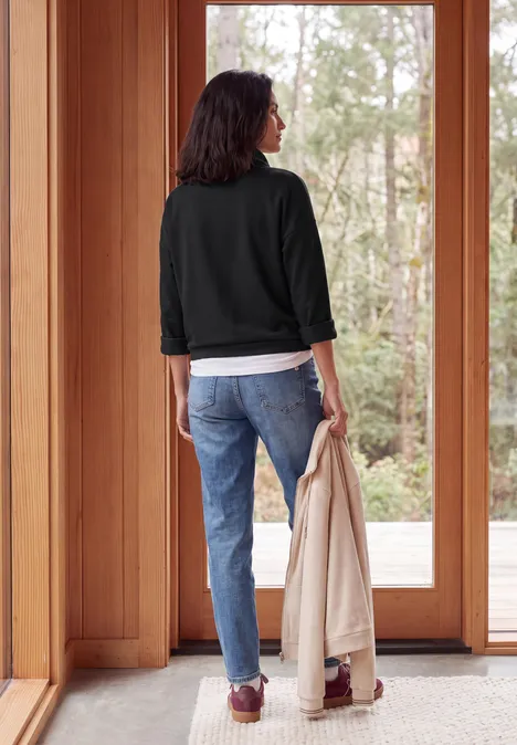 Shirt met lange mouwen, col en trekkoord Black Een persoon van achteren in jeans en jas houdt een mantel vast voor een glazen deur.