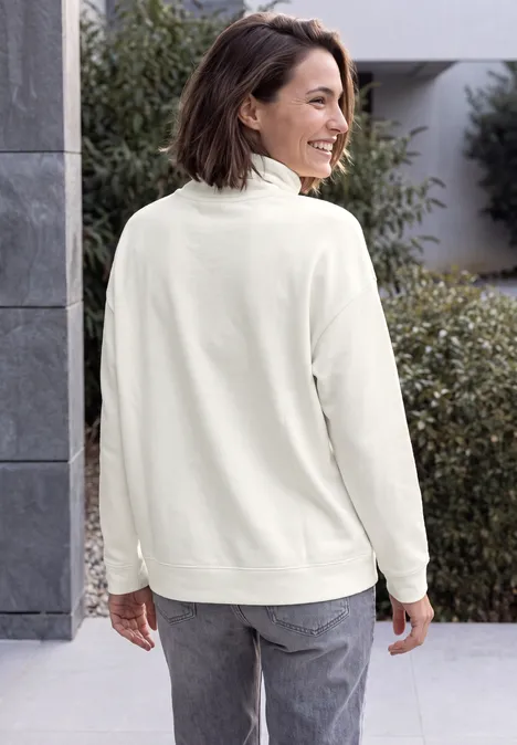 Shirt met lange mouwen, col en trekkoord vanilla white Vrouw in crème fleecevest en grijze jeans, glimlachend van opzij kijkend buiten.