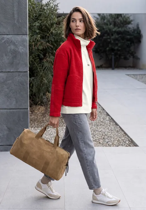 Shirt met lange mouwen, col en trekkoord vanilla white Vrouw in rode jas, grijze broek en witte sneakers draagt een bruine reisttas op het trottoir.