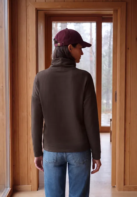 Langarm Shirt mit Rollkragen und Tunnelzug truffle brown Rückansicht einer Person mit Baseballcap und dunkler Fleecejacke vor großen Holzfenstern.