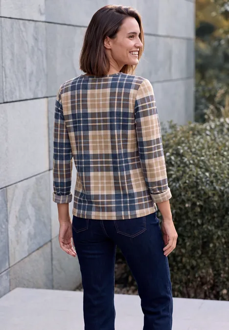 Shirt met lange mouwen, ronde hals en ruitjespatroon urban dark blue Eine Frau mit braunen Haaren in karierter Bluse und dunkler Jeans steht lächelnd vor Mauer und Büschen.