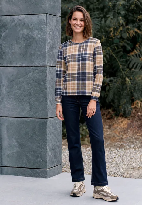 Shirt met lange mouwen, ronde hals en ruitjespatroon urban dark blue Eine Frau in kariertem Pullover und Jeans steht lächelnd vor einer grauen Wand und Grünpflanzen.