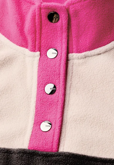 Nahaufnahme eines farbigen Fleece-Pullovers mit pinken Druckknöpfen auf beiger Stofffläche.